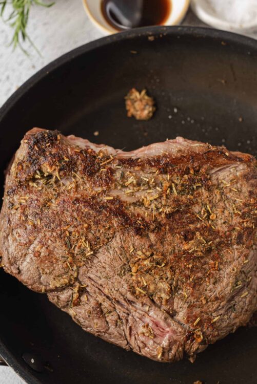 Gourmet searing prime rib roast with herbs in skillet for holiday dinner.
