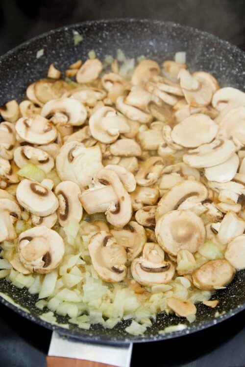 Sautéed mushrooms and onions in a black skillet, fresh ingredients for cooking.