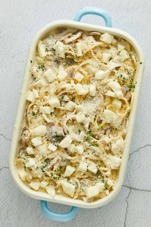 Creamy mushroom chicken pasta bake in a baking dish topped with cheese and herbs.