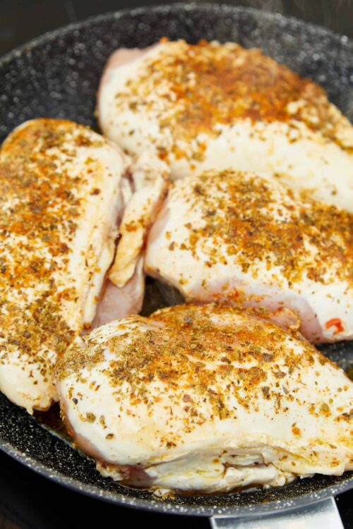 Juicy seasoned chicken breasts in a black skillet, seasoned with herbs and spices.