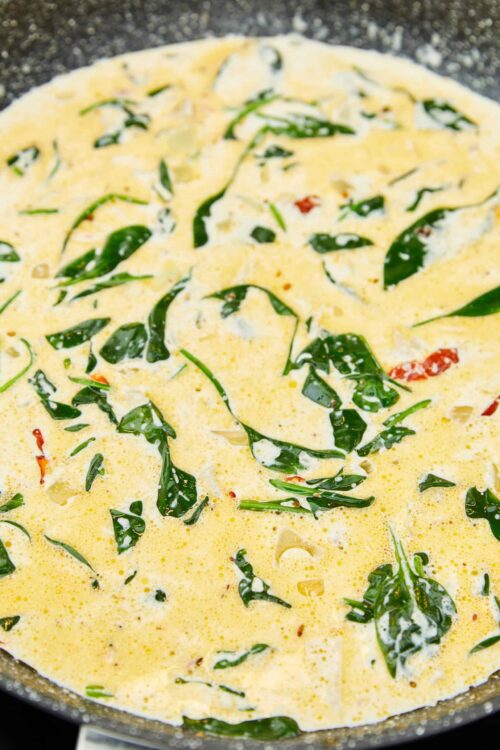 Fresh spinach and cherry tomato creamy scramble in a non-stick skillet.