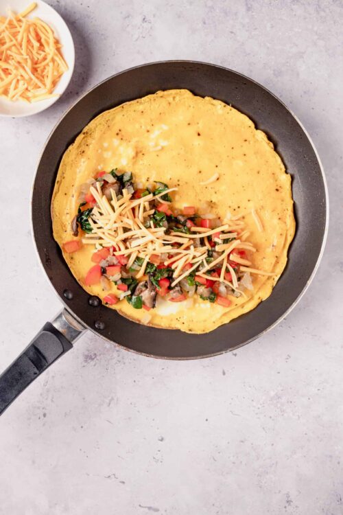 Creamy cheese omelette with sautéed vegetables in a black skillet, perfect for breakfast or brunch.