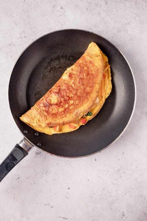 Scrambled egg omelette with filling on a non-stick frying pan.