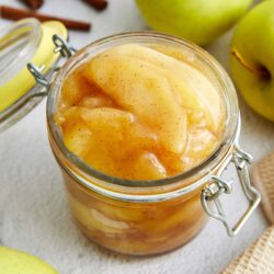 Cinnamon spiced apple compote in a glass jar with fresh green apples around it.