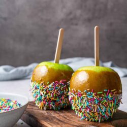 Sweet caramel apples with colorful sprinkles on a rustic wooden board.