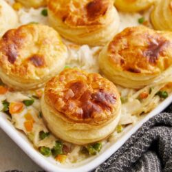 Flaky sausage gravy biscuits with creamy vegetable casserole on white dish, baked breakfast recipe.