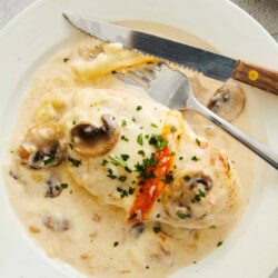 Creamy chicken and mushroom stew with herbs in a white bowl, served with a fork and knife.