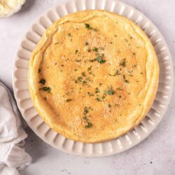 Creamy cheese quiche with golden crust garnished with chopped herbs. Perfect savory baked good from Baked Bree.