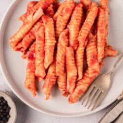 Crispy crinkle-cut sweet potato fries on white plate with peppercorns and fork.