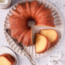 Light golden vanilla Bundt cake on white scalloped platter with sliced pieces.