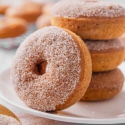 Buttermilk donuts coated with sugar, stacked on a white plate.