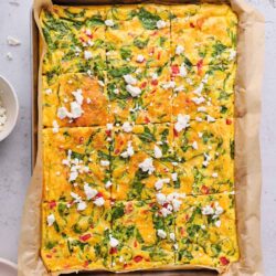 Scrambled egg casserole with fresh vegetables and feta cheese in a baking dish.