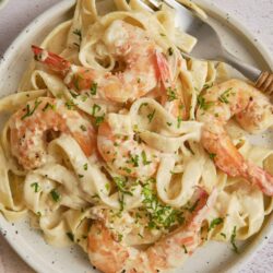 Creamy shrimp alfredo pasta with fresh herbs on a white plate.