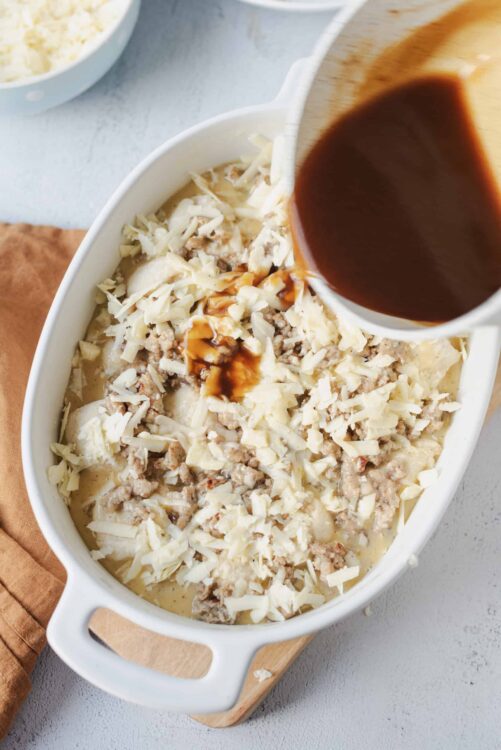 Creamy chicken and cheese casserole with gravy being poured on top.