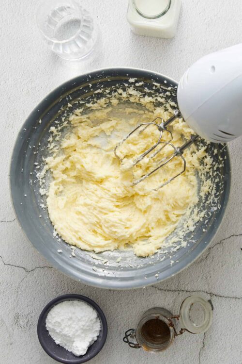 Creamy homemade butter in a mixing bowl with electric hand mixer, on a light textured surface.