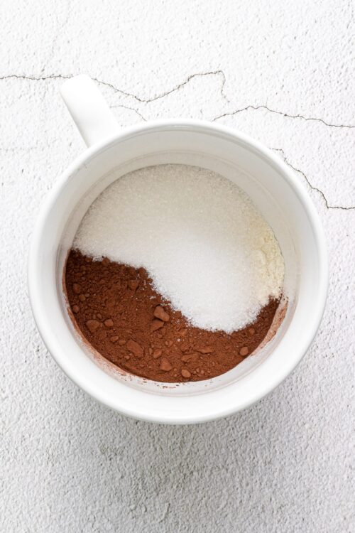 Coffee powder, sugar, and cocoa powder in a white mug for baking or chocolate recipes.