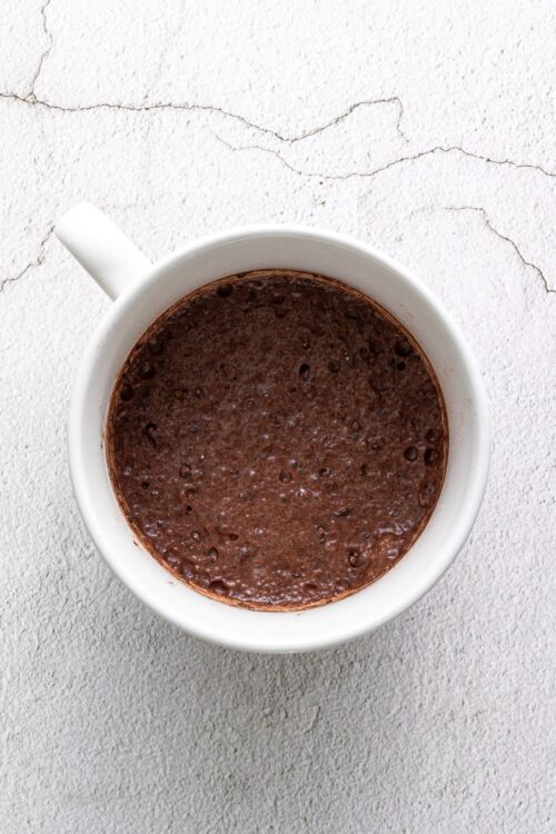 Rich, creamy hot chocolate in a white mug on a textured surface. Perfect for cozy fall and winter days.