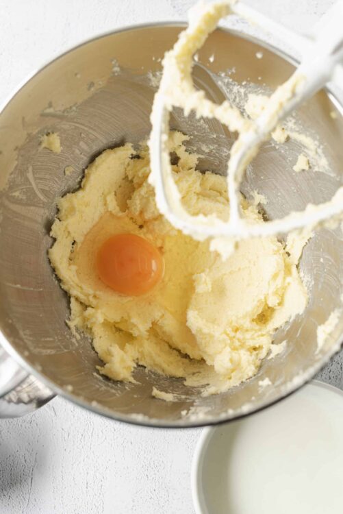 Creamy butter and sugar mixture with an egg in a stand mixer, ready for baking.