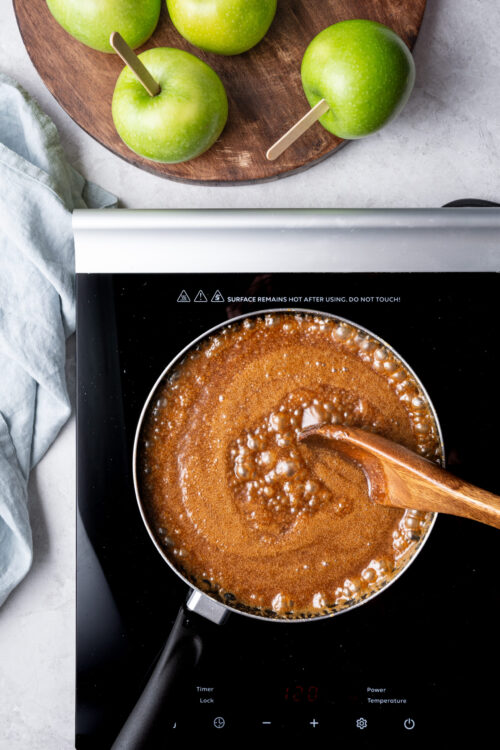 Fresh green apples with popsicle sticks, on a wooden tray, ready for making apple desserts or snacks.