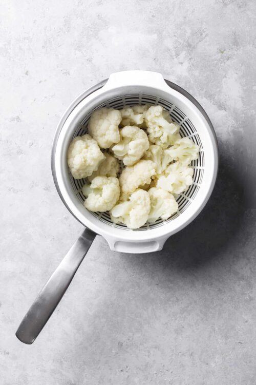 Whole cauliflower florets in a white steamer basket for healthy cooking.