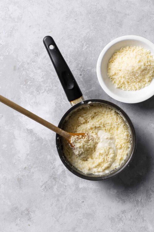 Creamy mashed potatoes with shredded cheese in a saucepan and cheese in a bowl.