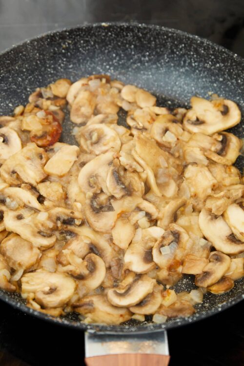 Sautéed sliced mushrooms with onions in a black skillet for flavorful cooking.
