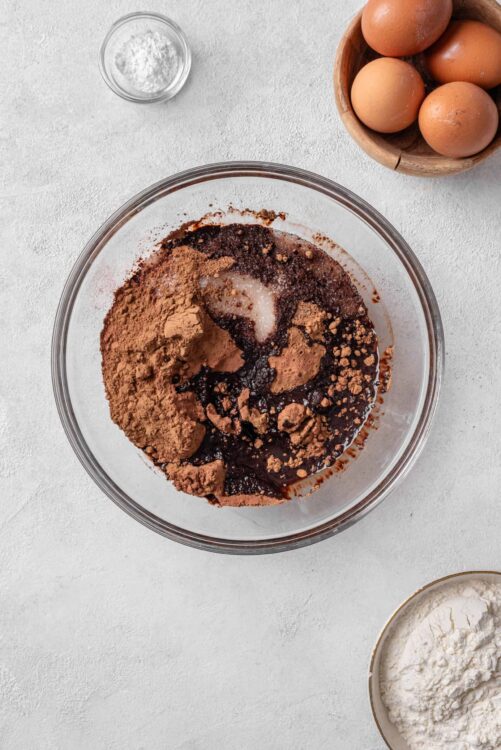 Rich chocolate cake batter with cocoa powder and eggs in a glass mixing bowl.