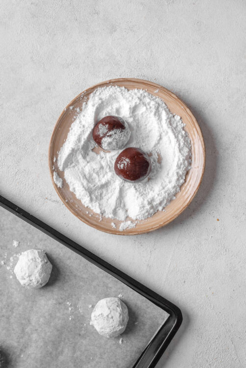 Powdered sugar-dusted chocolate truffles on a wooden plate, ready for indulgence.