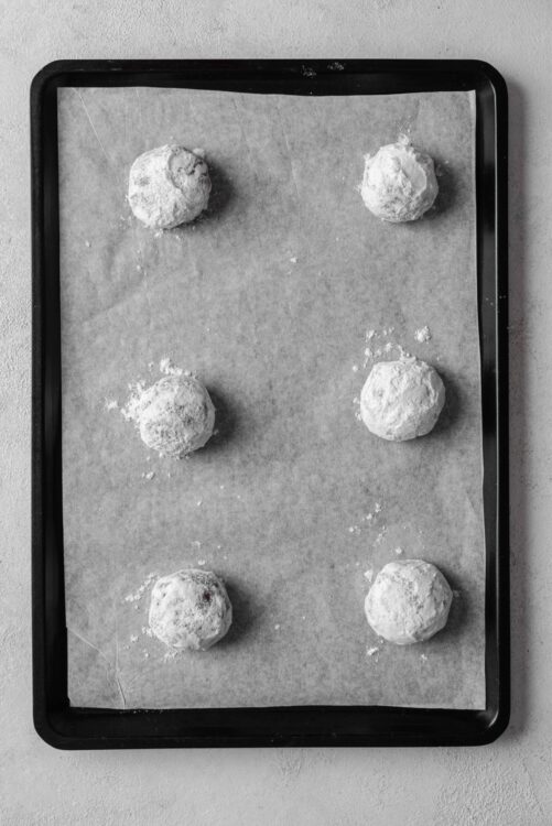 Dough balls dusted with flour on baking sheet for cookies.