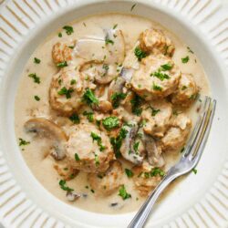 Creamy chicken and mushroom recipe in a white bowl with parsley garnish.
