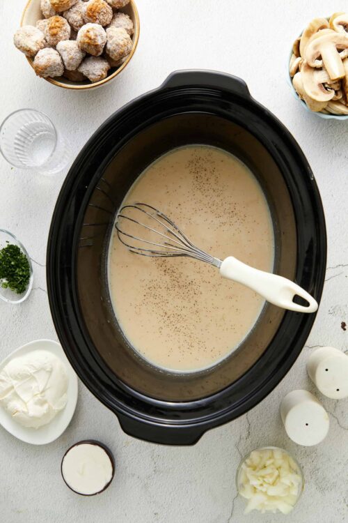 Creamy mushroom soup in slow cooker with ingredients around it, ready to cook.