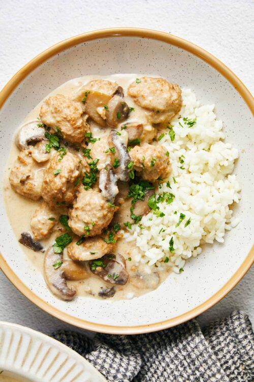 Creamy chicken and mushroom stroganoff served with white rice in a beige bowl.