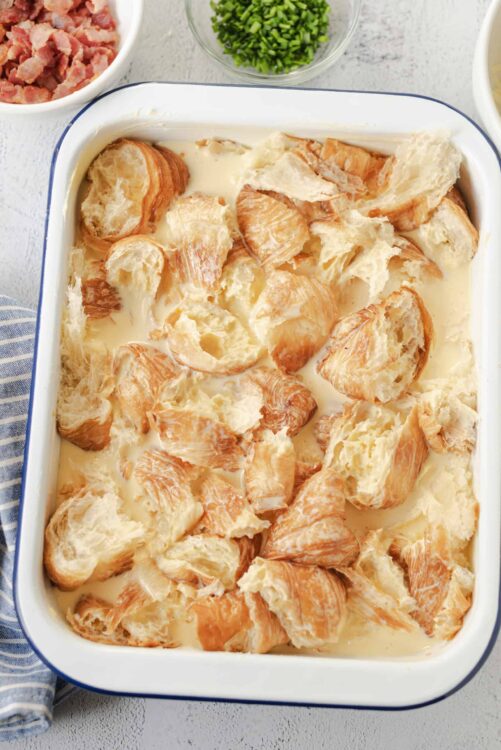 Golden baked bread pudding with creamy vanilla custard in a white baking dish. Perfect comfort dessert.