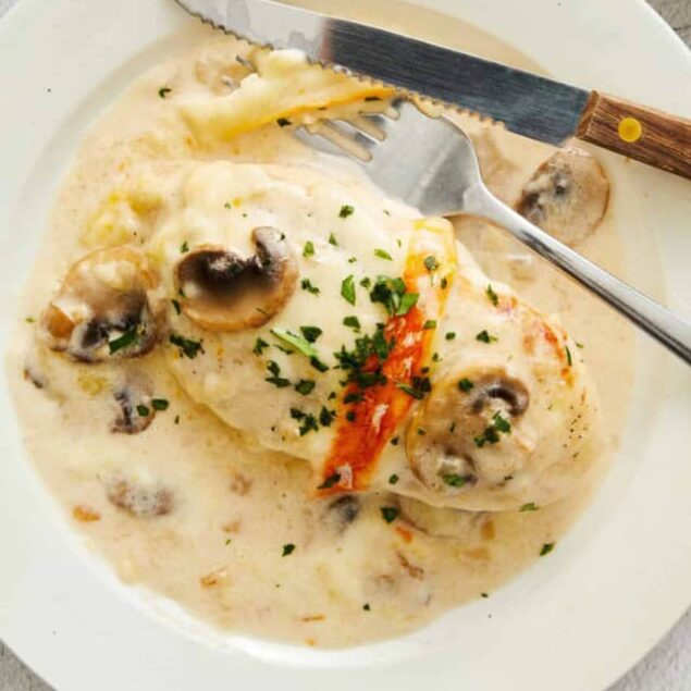 Creamy chicken and mushroom skillet with herbs and vegetables, served in a white bowl.