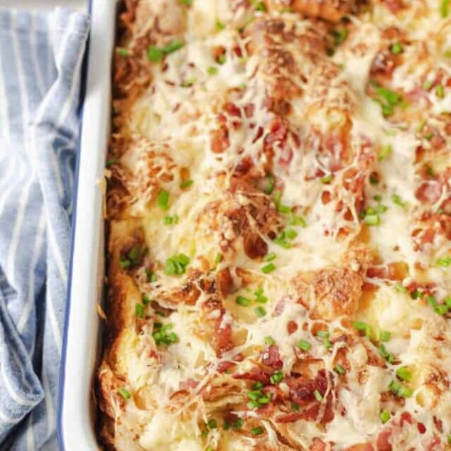 Baked cheesy lasagna casserole with tomatoes and green onions in white baking dish.