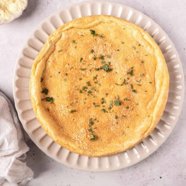 Golden baked quiche with herbs on a white plate, ready to serve.