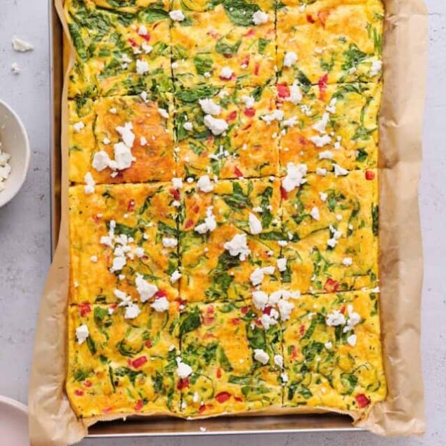 Savory vegetable frittata topped with cheese and herbs in baking dish.