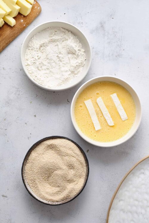 Flour, eggs, and breadcrumbs on a white surface for baking recipes.