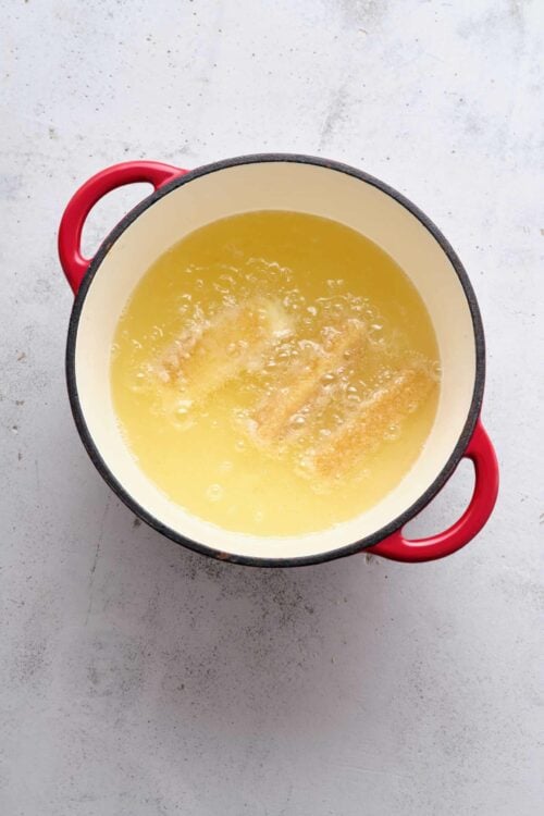 Buttery melted butter in a red-handled saucepan on a textured white surface.