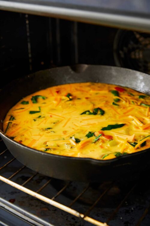Baked Bree, cheesy vegetable frittata cooking in a cast iron skillet in the oven.