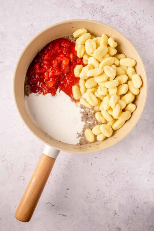 Cream of tomato and pasta sauce in a beige skillet with a wooden handle.