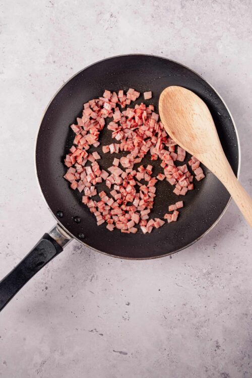 Diced cooked bacon sizzling in a black frying pan.