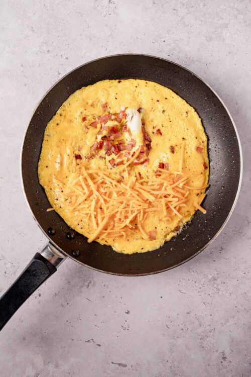 Creamy scrambled eggs with cheese and bacon in a non-stick skillet.