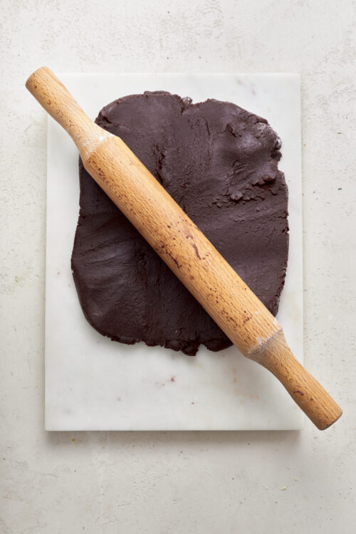 Raw chocolate dough with a rolling pin on a marble board, for baking and confectionery recipes.