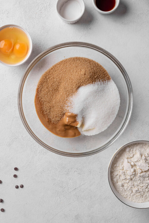 Flour, sugar, brown sugar, eggs, and mixing ingredients for baking on a white surface.