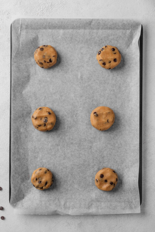 Soft chocolate chip cookie dough balls on baking parchment ready to bake.