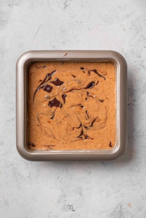 Creamy chocolate chip cookie dough in a square metal baking pan.