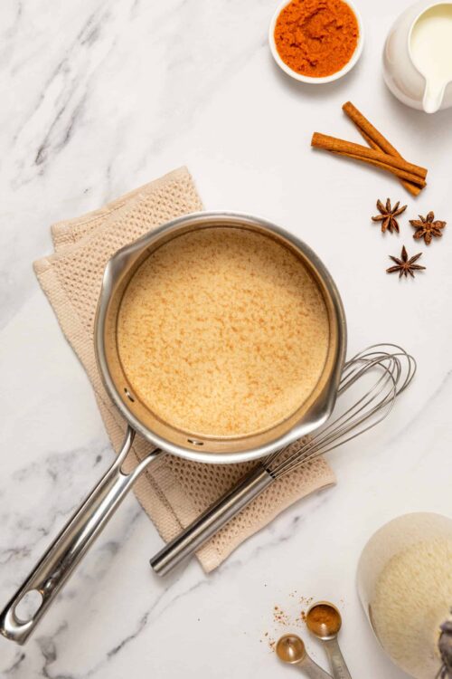 Creamy homemade butterscotch sauce in a stainless steel saucepan on a marble countertop.