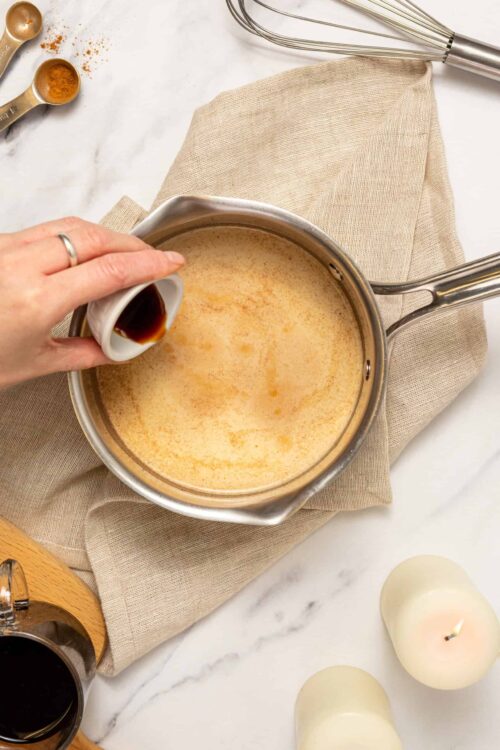 Creamy homemade vanilla custard in a stainless steel saucepan on a marble surface, with vanilla bean and measuring spoons.