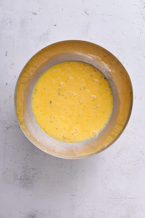 Creamy scrambled eggs in a stainless steel mixing bowl, ready to cook.